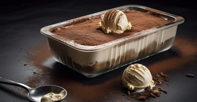 Overhead shot of creamy Tiramisu Ice Cream in a pan with cocoa powder dusting and a scoop removed.